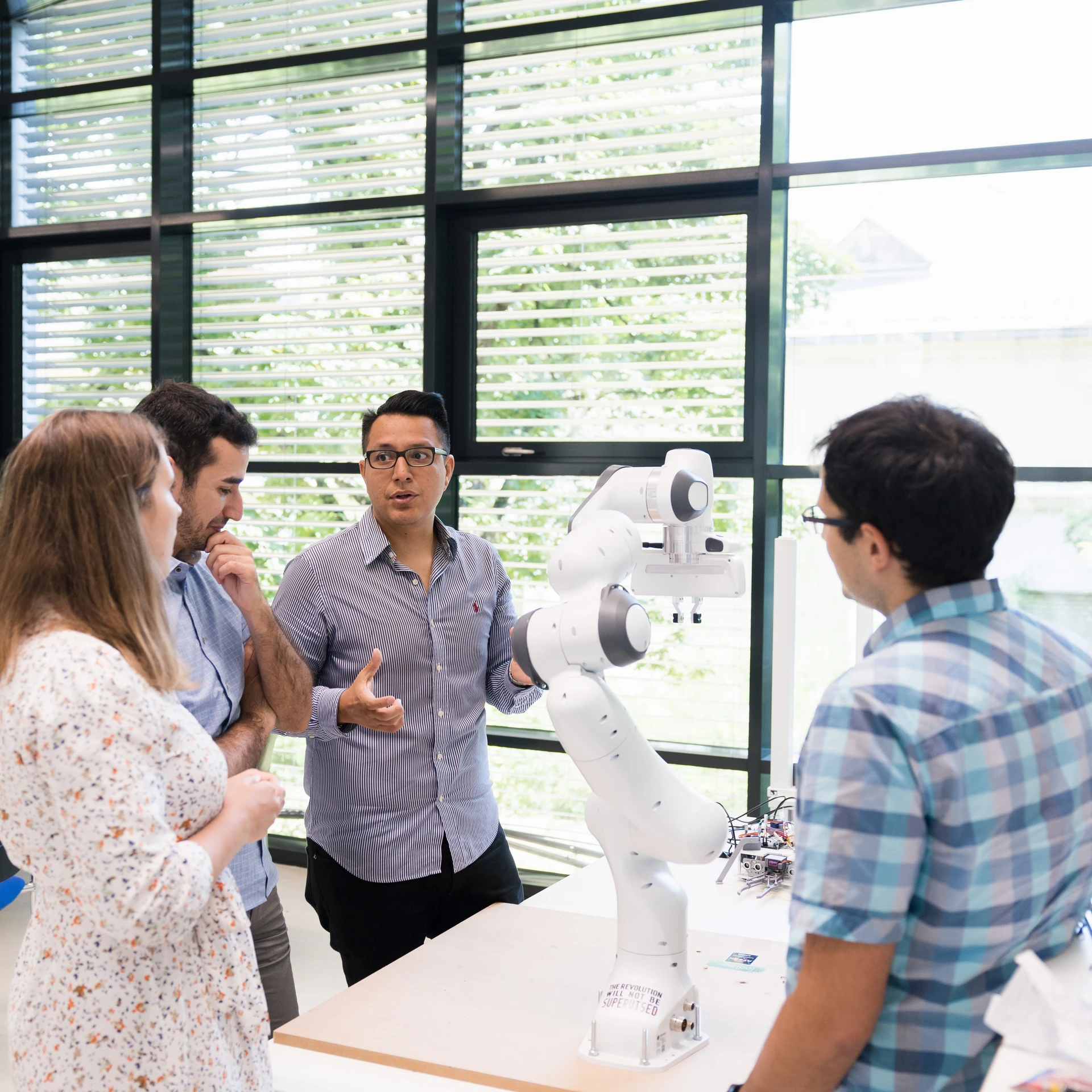 Team steht um einen Roboter-Arm, der auf einem Tisch steht versammelt